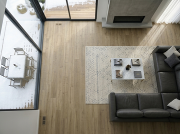 Ceaser SPC vinyl flooring, overhead view beside a dark sectional sofa and patterned rug.